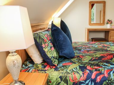 A bedroom with a bed featuring floral bedding and pillows a wooden vanity with a mirror and a table lamp at Holly Lodge in Forden near Montgomery