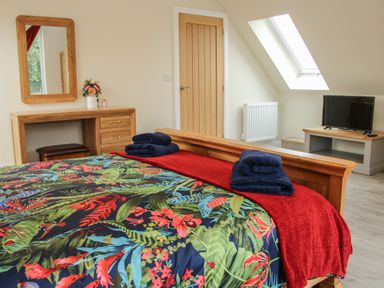 A bedroom with a wooden bed with floral bedspread folded towels a dressing table with a mirror flowers a skylight window and a TV at Holly Lodge in Forden near Montgomery