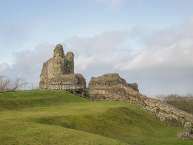 Ruins of a stone castle on a grassy hill with a wooden walkway and railings at Holly Lodge in Forden near Montgomery