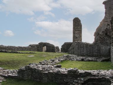 Ancient stone ruins with partial walls and a tall cylindrical tower under a cloudy sky