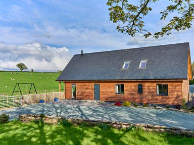 A wooden house with a pitched roof and skylights in a rural area with a gravel driveway and a swing set at Holly Lodge in Forden near Montgomery