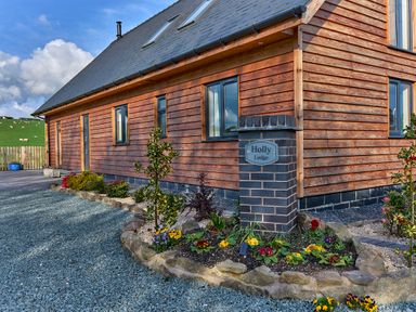 A wooden house with a garden bed and a brick pillar with a sign reading Holly Lodge in Forden near Montgomery