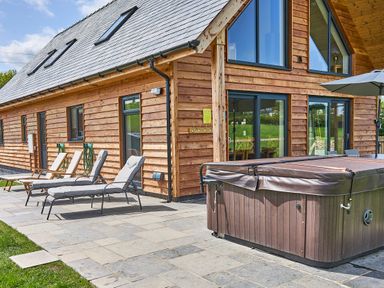 An outdoor patio area with lounge chairs and a covered hot tub next to a wooden house at Holly Lodge in Forden near Montgomery