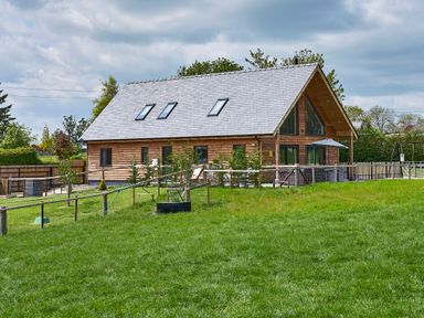 A wooden house with skylights and a fenced yard on a grassy hill at Holly Lodge in Forden near Montgomery