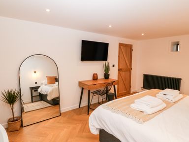 A bedroom with a bed, a wooden desk, a wall-mounted TV, a large mirror, a potted plant, and a wooden door at Sgubor in Llangefni