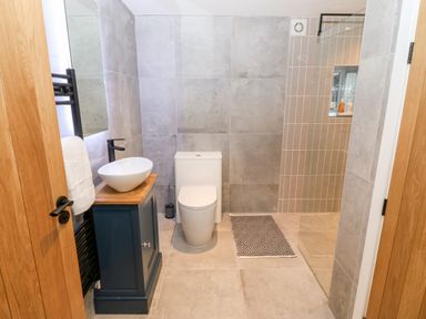 A bathroom with a toilet a sink on a cabinet a mirror and a walk in shower at Sgubor in Llangefni