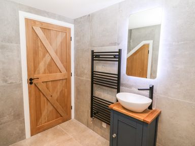 A bathroom with a wooden door a black towel radiator a blue vanity unit with a white basin and a rectangular mirror at Sgubor in Llangefni