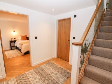 A hallway with a carpet and stairs next to a wooden door and an open door to a bedroom at Sgubor in Llangefni