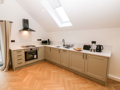 A kitchen with beige cabinets a built-in oven gas stove microwave and skylight at Sgubor in Llangefni