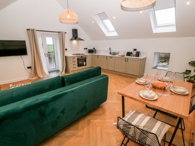 An open kitchen and dining area with green sofa wooden dining table set with plates and glasses at Sgubor in Llangefni