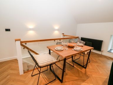 A dining area with a wooden table set for four and black chairs with cushions near a staircase at Sgubor in Llangefni