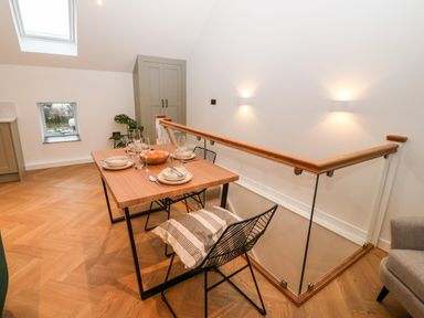 A dining table set for four with plates and glasses next to a glass railing and staircase at Sgubor in Llangefni