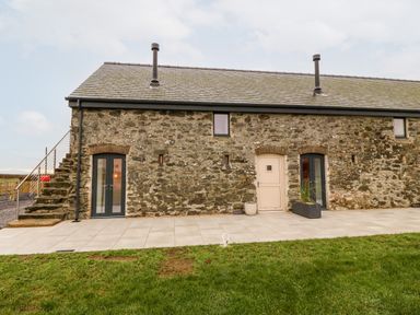 Exterior of a stone house with three doors two black framed glass doors one beige door and stone steps on the left at Sgubor in Llangefni
