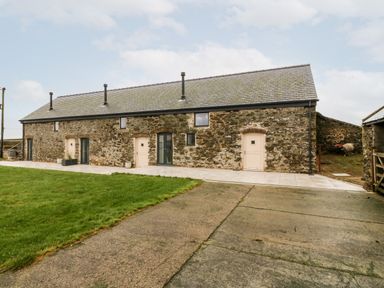 Exterior view of a stone building with multiple doors and windows next to a grassy area at Sgubor in Llangefni