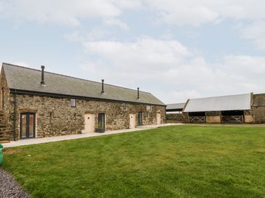A stone building with multiple doors and windows next to a grassy area at Sgubor in Llangefni