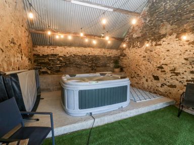 An indoor area with a hot tub on a raised concrete platform surrounded by stone walls and string lights at Sgubor in Llangefni