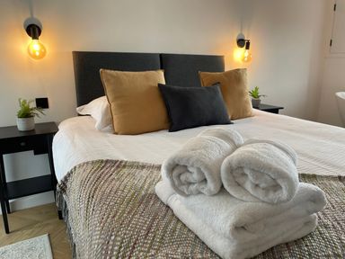 A bedroom with a bed with three pillows two bedside tables with lamps and plants and folded towels on the bed at Sgubor in Llangefni