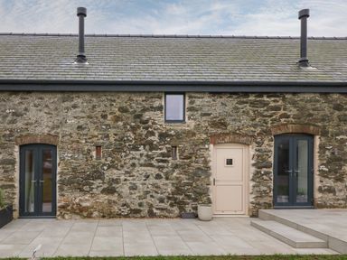 Exterior view of a stone building with a beige door and two dark gray French doors at Beudy in Llangefni