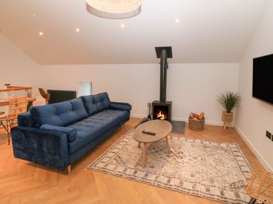 A living room with a blue sofa a coffee table a fireplace a rug and a television at Beudy in Llangefni