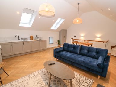 An open plan living space with a blue sofa wooden coffee table kitchen cabinets and dining table with chairs at Beudy in Llangefni