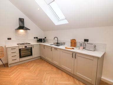 A kitchen with light grey cabinets and wooden floor under a skylight at Beudy in Llangefni