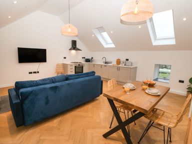 An open plan kitchen and dining area with a blue sofa a wooden dining table with chairs and kitchen appliances at Beudy in Llangefni