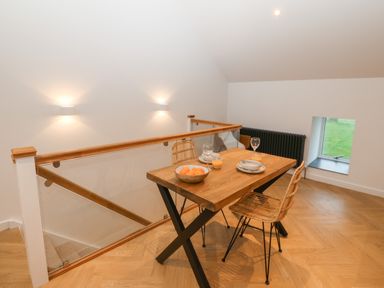 A dining area with a wooden table and two rattan chairs near a staircase with glass railing at Beudy in Llangefni