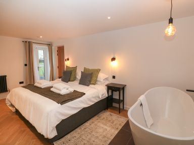 A bedroom with a double bed pillows bedside tables and a bathtub at Beudy in Llangefni