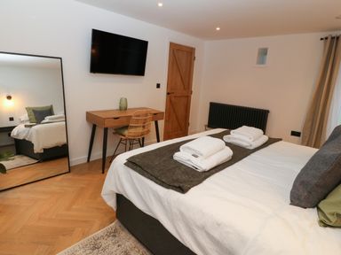 A bedroom with a bed with folded towels a desk with a chair a wall-mounted TV a wooden door and a full-length mirror at Beudy in Llangefni