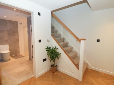 A staircase with a glass railing and a potted plant next to a doorway leading to a bathroom with a toilet and tiled walls at Beudy in Llangefni