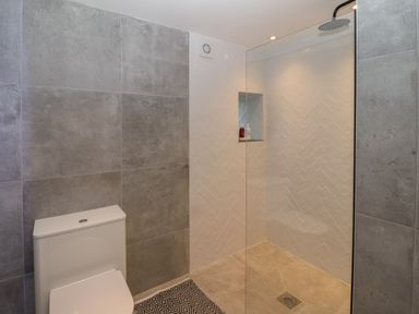 A bathroom with a toilet and a walk-in shower with tiled walls and a glass partition at Beudy in Llangefni