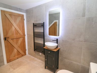 A bathroom with a wooden door a black towel rack a small cabinet with a sink and a backlit mirror at Beudy in Llangefni
