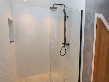A walk in shower with black fixtures glass divider and white herringbone tiled walls at Beudy in Llangefni