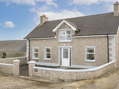 A pebble dash house with a white door three windows a slate roof and a low surrounding wall at Grannys in Bushmills County Antrim