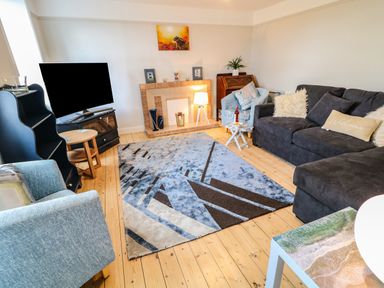 A living room with a blue patterned rug a grey sofa a blue armchair a television and a fireplace at Granny's in Bushmills County Antrim