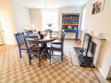 A dining room with a round table and six chairs next to a fireplace and a blue cabinet at Granny's in Bushmills County Antrim