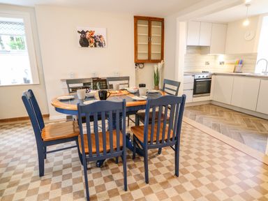 A dining area with a wooden table and six chairs set with plates and cups next to a kitchen with white cabinets and an oven at Granny's in Bushmills County Antrim