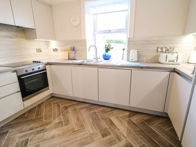 A kitchen with white cabinets a built in oven a sink under a window and appliances at Granny's in Bushmills County Antrim