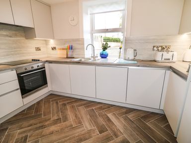 A kitchen with white cabinets wooden countertops a window a sink a blue vase with green leaves a kettle a toaster and a cooktop at Granny's in Bushmills County Antrim