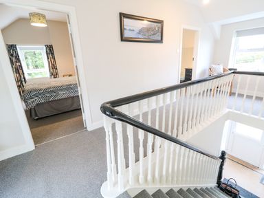A stairway landing with white banisters and black handrail connecting to carpeted rooms with windows at Granny's in Bushmills County Antrim