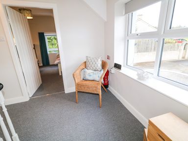 A corner with a wicker chair and cushions next to a large window and a door to a bedroom at Granny's in Bushmills County Antrim