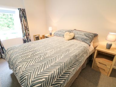 A bedroom with a bed covered with patterned bedding two bedside tables with lamps and a window with curtains at Grannys Bushmills County Antrim