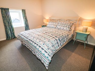 A bedroom with a patterned bedspread a bed with a headboard two bedside tables with lamps and a window with curtains at Grannys in Bushmills County Antrim