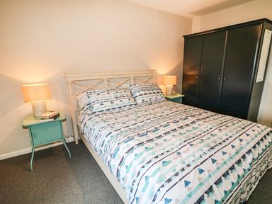 A bedroom with a bed a patterned bedspread two bedside tables with lamps and a black wardrobe at Granny's Bushmills County Antrim