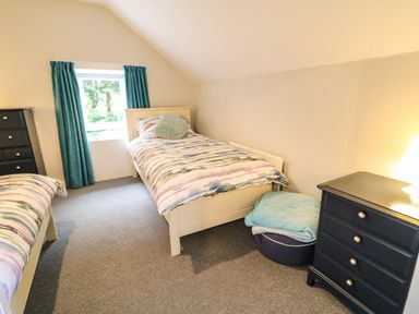 A bedroom with two single beds a window with teal curtains a black chest of drawers and a soft round cushion at Grannys in Bushmills County Antrim