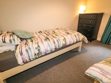 A bedroom with a single bed with patterned bedding a black chest of drawers and a lit lamp at Grannys in Bushmills County Antrim