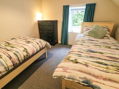 A bedroom with two single beds a black chest of drawers and a window with green curtains at Granny's in Bushmills County Antrim