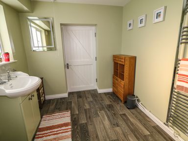 A bathroom with a white sink cabinet a wooden storage unit a door and a striped rug at Granny's in Bushmills County Antrim