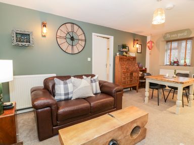 A living room with a brown leather sofa and a wooden coffee table and a dining table with chairs at Cwm Caeth Cottage in Nantmor near Beddgelert