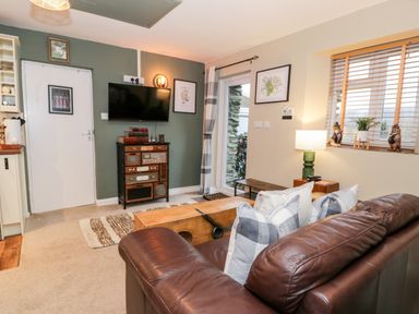A living room with a brown leather sofa pillows a wooden chest and a TV on the wall at Cwm Caeth Cottage in Nantmor near Beddgelert